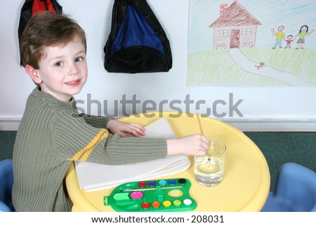Handsome and happy little boy sitting in a pre-school.  Drawing on wall not copyrighted.
