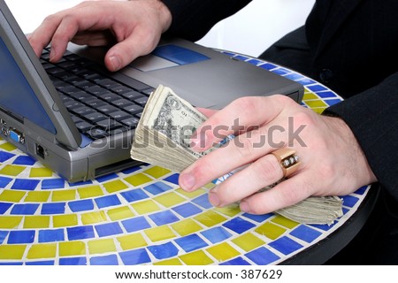 Cash in Man's Hand Resting On Table Top Near Laptop.