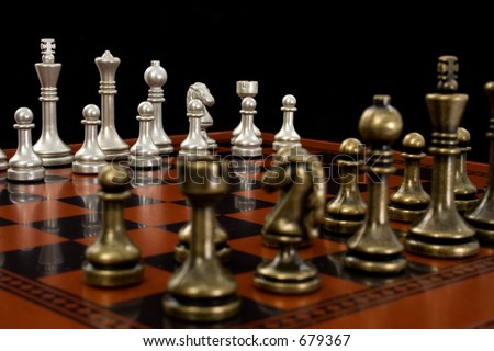 Wooden chess board with metal peices.  Shot in studio on black from corner to corner.  Focus on light pieces.