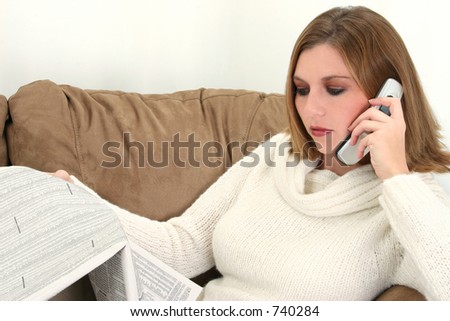 Beautiful twenty-five year old woman on cellphone with stock pages. Sitting on couch.  Shot in studio.