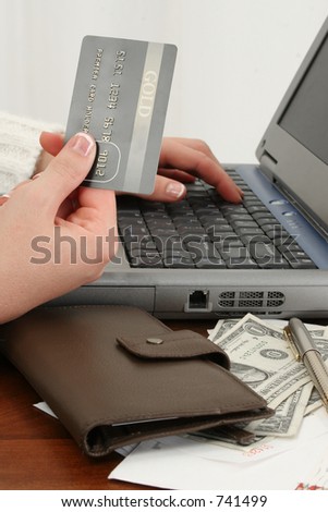 Woman\'s hand with credit card at laptop.  Bills, money, checks on table beside her. Shot in studio.
