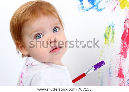 Beautiful little redhead baby painting at poster board.  Bright blue eyes and red hair. Shot in studio.