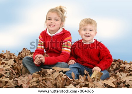 Brother and Sister in red sweaters sitting in big pile of leaves.