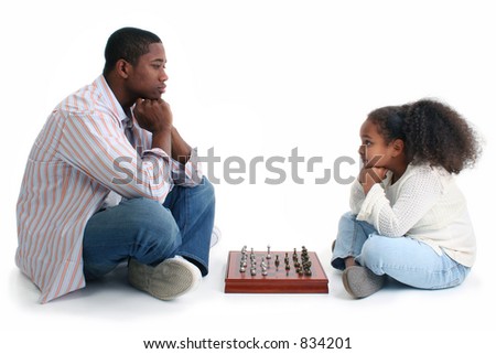 African American man and little girl playing chess.  Sitting crossed-legged on either side of game and looking at each other.  Shot in studio over white.