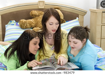Three teen girls looking through the school yearbook.  At sleep over, wearing pajamas.