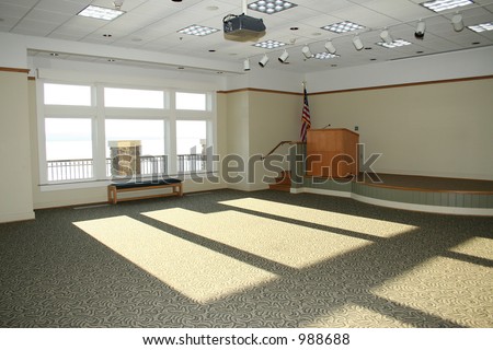 Large empty meeting room with stage, podium, American Flag.