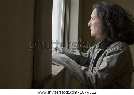 Thirty-eight year old woman looking out the window of impoverished home. Hopeless expression on face.