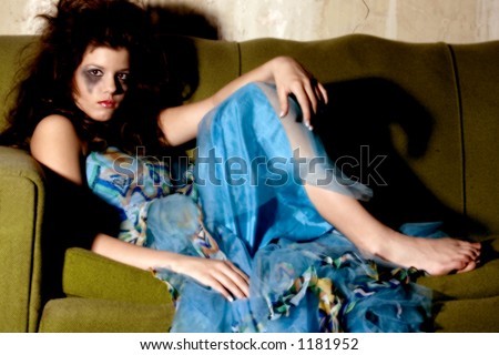 Young woman in formal dress and goth make-up sitting on old couch.