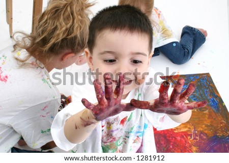 Adorable toddler boy looking at hands covered in paint.