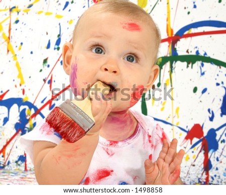 Beautiful baby covered in bright paint with paint brush in mouth.