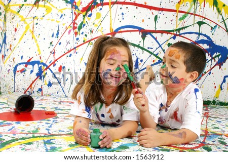 Adorable boy and girl covered in paint lying on splattered paint background