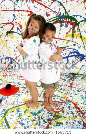 Adorable boy and girl covered in paint standing on splattered paint background; full body