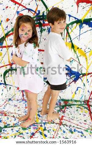 Adorable boy and girl covered in paint standing on splattered paint background; full body