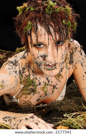 Beautiful 30 year old woman covered in mud and moss over black.