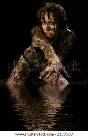 Beautiful 33 year old woman covered in mud and moss over black.