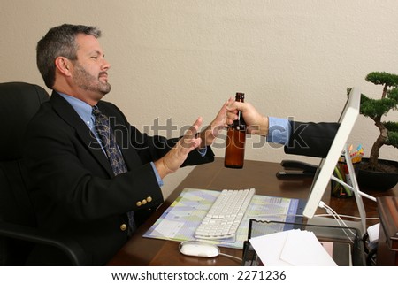 Business man saying no to a beer handed through computer screen at desk.