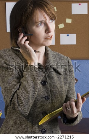 Thirty something year old woman in office taking notes wearing wireless communication piece in ear.