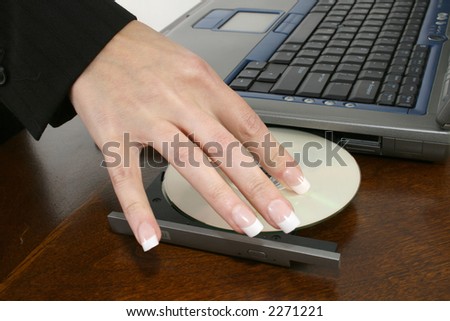Woman\'s hand placing dvd into laptop computer at desk.