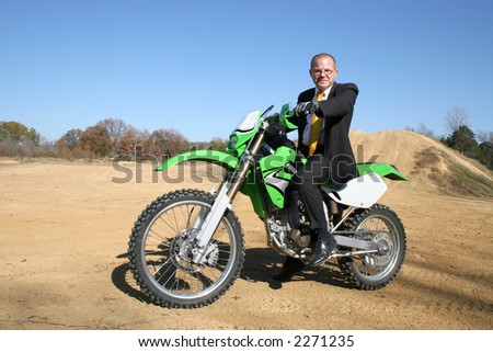 Thrity something business man in suit riding dirt bike on dirt riding track.
