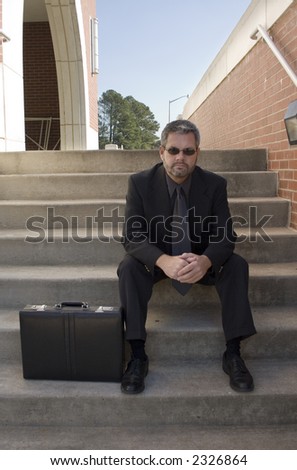 Fourty something business man sitting on steps outside office.  Briefcase and sunglasses.