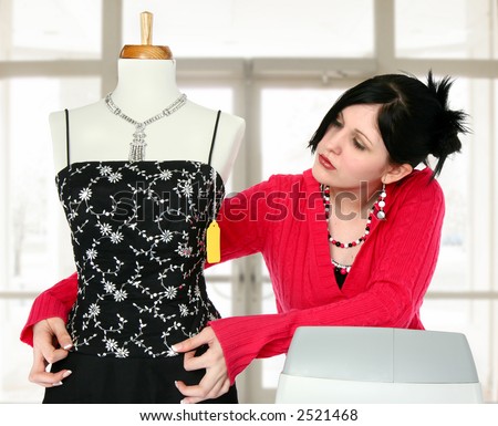 Young woman at cash register adjusting dress on mannequin.