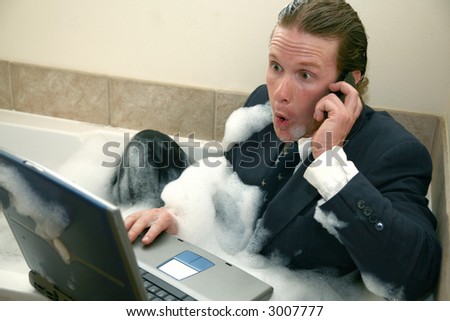 Thirty something business man in bubble bath with cellphone and laptop computer.