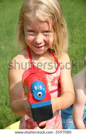 Beautiful six year old girl plays with water gun in kiddie pool.
