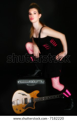 Beautiful Hispanic woman with electric guitar and amp over black.