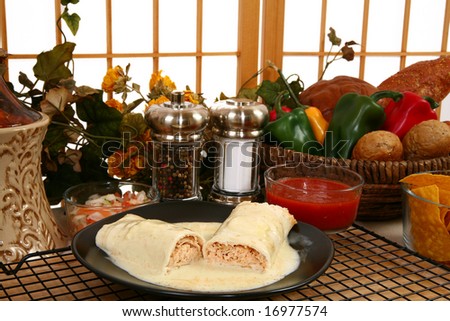 Chicken burrito in plate covered in cheese dip in kitchen or restaurant.
