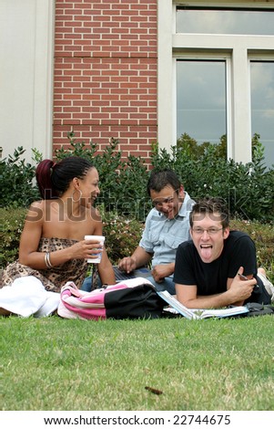 College students on campus.  Sitting in grass with books, coffee, bags.