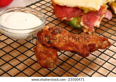 Hot spicy buffalo style chicken wings next to bowl of Blue Cheese dressing and sandwich.