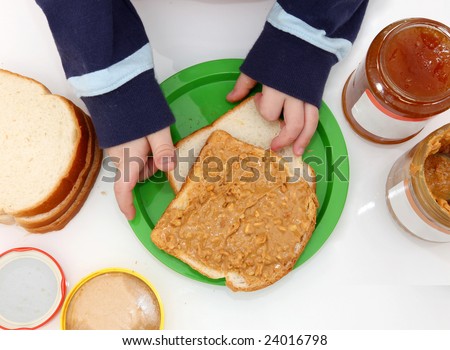 young child\'s hands making peanut butter and jelly sandwiches