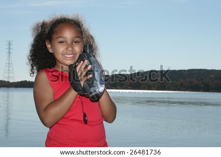 Adorable five year old African American Girl with camcorder at the lake.