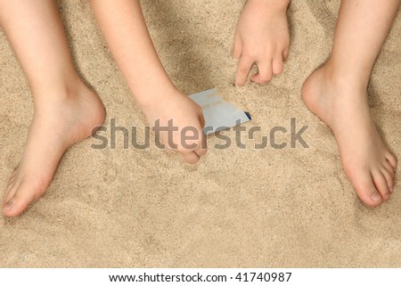 Young child's hands and feet in sand playing with credit card.