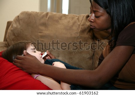 Beautiful African American woman taking temperature of sick girl laying on couch.