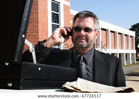 Attractive 40 year old business man in suit and sunglasses on phone outside.