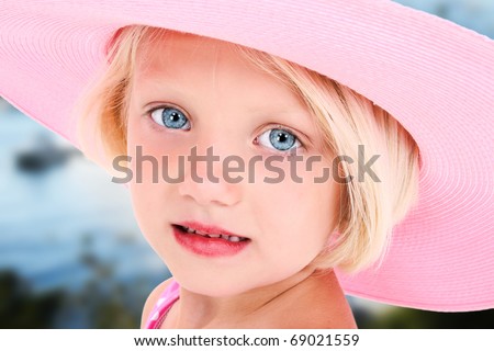 Beautiful five year old girl in big pink summer hat and blue eyes outside.