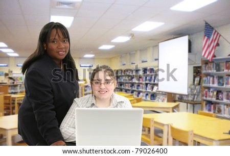 Smiling teacher and student in library together on laptop computer.