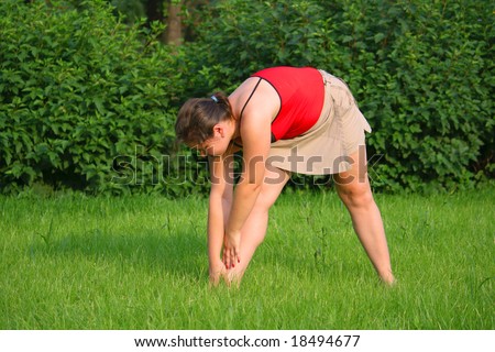 Girl doing exercise on grass. Bend to right leg