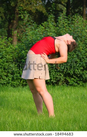 Girl doing exercise on grass. Bend back.