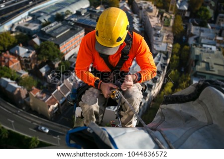 Close up pic of male rope access industrial worker wearing yellow hard hat, long sleeve shirt, safety harness, working, abseiling off from the high rise building at circular quay, Sydney, Australia