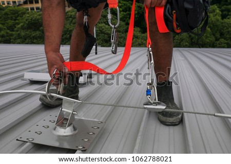 Male hand using transfer, clipping stainless industrial locking hook into the fall arrest roof anchor point systems, while tail is connected into his body personal safety harness in Sydney, Australia