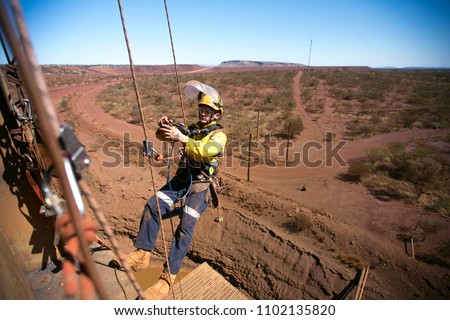 Rope access miner welder worker wearing fully safety equipment abseiling and sorting clipping his hard ling device into back up rope ready to weld on construction mine site Perth Western of Australia