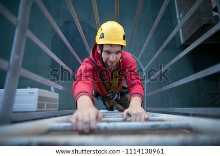 Male industry rope access worker wearing full safety harness, helmet climbing safety ladder at construction site in Sydney city high rise building, Australia