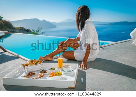 young woman at an infinity pool having breakfast looking out over ocean of Santorini, luxury break fast swim pool
