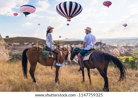 happy young couple on vacation Turkey Kapadokya horse riding in the mountains with hot air balloons on the background of Cappadocia Goreme