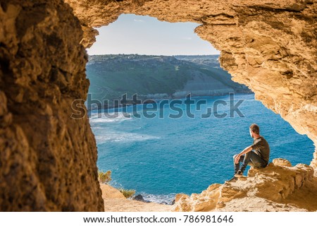 Gozo island Malta, young man and a View of Ramla Bay, from inside Tal Mixta Cave Gozo looking out over the blue ocean on a bright day