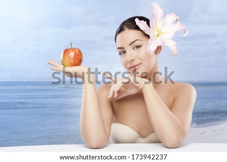 Beautiful, sensual woman on seaside with apple in hand and flower in hair