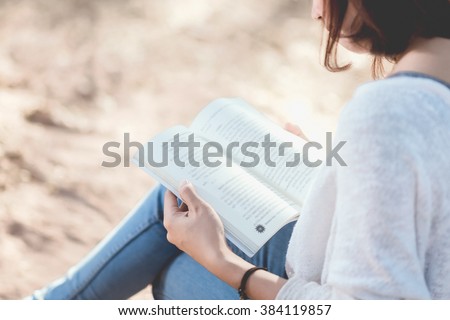 A young woman reading a book. Book in woman hands. Woman reading a book in park.