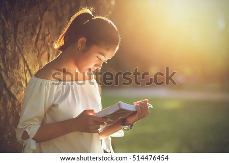 Asian girl reading book at park in summer sunset light. asian woman reading book in Thailand. asian Beautiful woman reading a book at big tree in park.